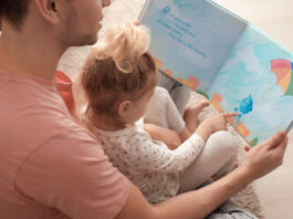Father and his daughter reading book on floor in children room