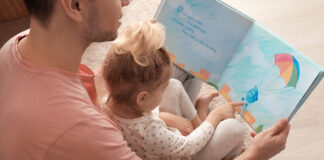 Father and his daughter reading book on floor in children room