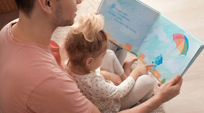 Father and his daughter reading book on floor in children room