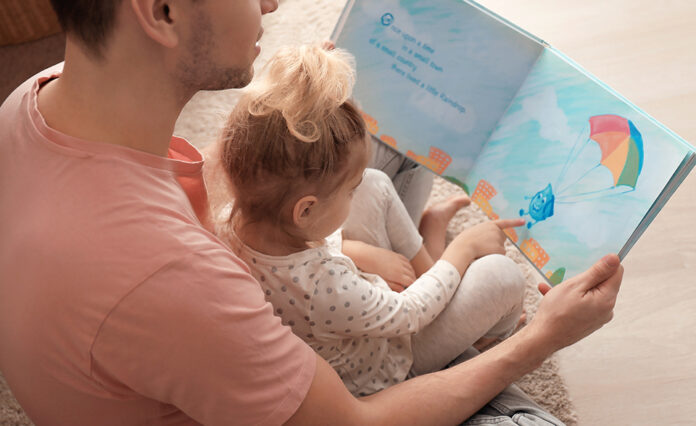 Father and his daughter reading book on floor in children room