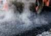 Heavy industrial steamroller machine pressing hot, steaming black asphalt during road construction