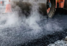 Heavy industrial steamroller machine pressing hot, steaming black asphalt during road construction
