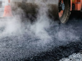 Heavy industrial steamroller machine pressing hot, steaming black asphalt during road construction