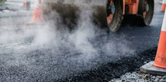 Heavy industrial steamroller machine pressing hot, steaming black asphalt during road construction