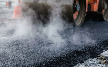 Heavy industrial steamroller machine pressing hot, steaming black asphalt during road construction