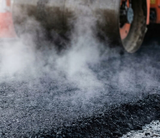 King City begins pavement rehabilitation project Heavy industrial steamroller machine pressing hot, steaming black asphalt during road construction