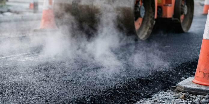 Asphalt roadwork AdobeStock_1971405188 Heavy industrial steamroller machine pressing hot, steaming black asphalt during road construction