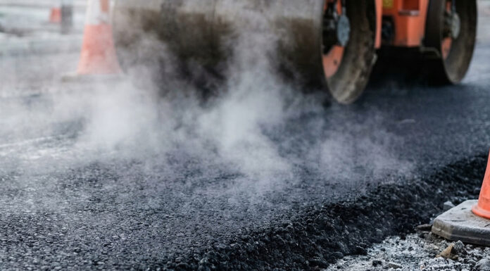 King City begins pavement rehabilitation project Heavy industrial steamroller machine pressing hot, steaming black asphalt during road construction